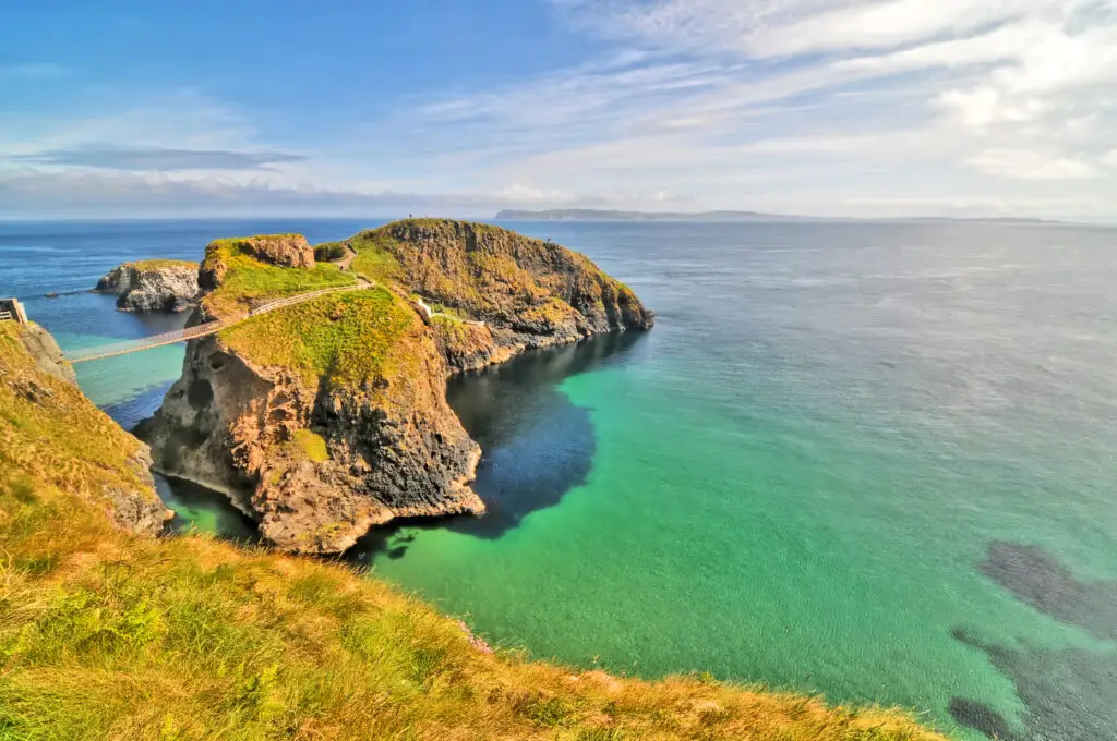 Carrick-a-Rede Rope Bridge in Northern Ireland, a scenic view of the iconic suspension bridge linking the mainland to Carrick-a-Rede island over a turquoise sea.